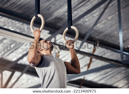 Fitness, exercise man in gymnastics gym during pull up, training or exercise on rings. Young sports athlete or gymnast, strong mindset and start workout to improve muscle or cardio at sport club