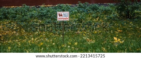 Sign with picture of dog on lawn, sign with inscription in Russian: dog walking is prohibited. Green grass with yellow fallen leaves. Horizontal banner. Take care of nature in city, take care of pets.