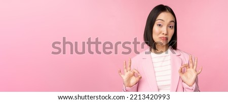 Not bad. Impressed businesswoman, asian office lady showing okay sign and nod in approval, standing over pink background