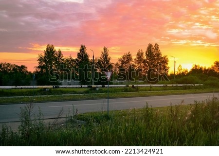 Yield sign on the background of the road and trees against the backdrop of a bright beautiful dawn and a pink morning sky