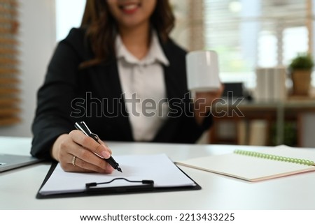 Close up view of woman signing document on white office desk. Focus on female hand