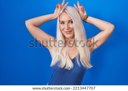 Caucasian woman standing over blue background posing funny and crazy with fingers on head as bunny ears, smiling cheerful 