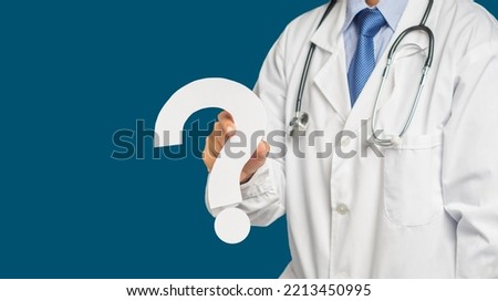 Midsection of a doctor in uniform holding a white question mark while standing on a blue background. Space for text. Healthcare concept