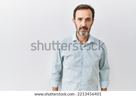 Middle age hispanic man with beard standing over isolated background relaxed with serious expression on face. simple and natural looking at the camera.  Royalty-Free Stock Photo #2213456401