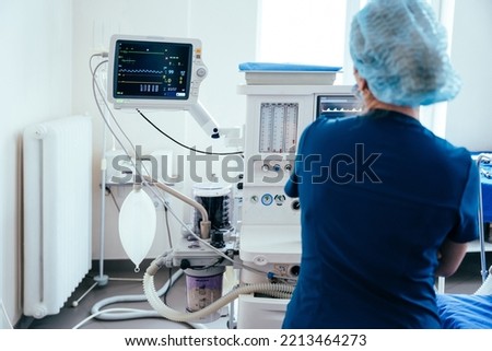 Rear view of female anaesthesiologist with monitor during operating in operation room. Modern equipment in clinic. Emergency room. Royalty-Free Stock Photo #2213464273