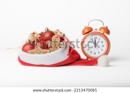 Conceptual photo of meeting the new year, alarm clock and Christmas tree decorations in Santas hat isolated on background.