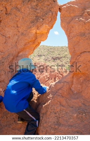 A boy in sports clothes and climbing over a rock made of orange clay against the background of the sky and the green horizon.Sports healthy childhood.