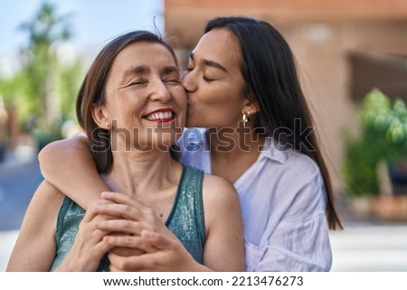 Two women mother and daughter hugging each other kissing at street
