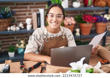 Young beautiful hispanic woman florist using laptop reading document at florist Royalty-Free Stock Photo #2213476727
