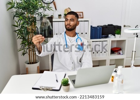 Young arab man wearing doctor uniform holding xray at clinic