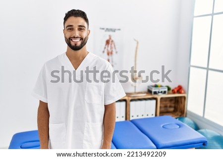 Young handsome man with beard working at pain recovery clinic with a happy and cool smile on face. lucky person.  Royalty-Free Stock Photo #2213492209