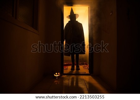 Halloween concept. Creepy silhouette in the dark corridor with pumpkin head. Toned light with fog on background. Selective focus. Long shutter shot