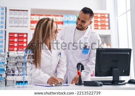 Man and woman pharmacist smiling confident writing on document at pharmacy