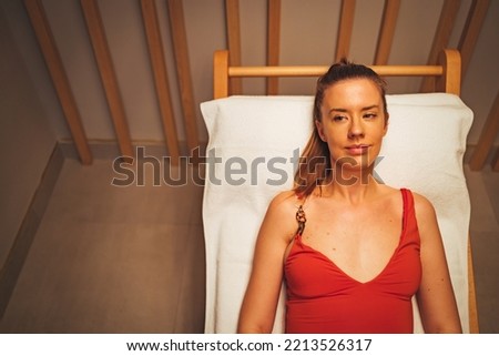 Young woman sitting on bench in infrared sauna, space for text. Spa treatment. Young woman resting in Infra sauna.  Relaxing in sauna during wellness weekend.