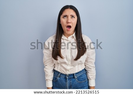 Young latin woman standing over blue background angry and mad screaming frustrated and furious, shouting with anger. rage and aggressive concept. 