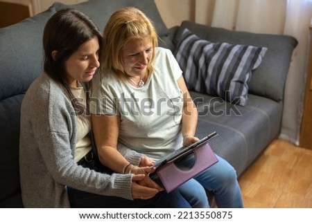 Mother and daughter on the sofa at home while looking at the tablet and being happy.