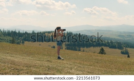 Young photographer shooting landscape on beautifull green hillway, taking pictures of nature. Girl filling the portfolio with amazing pictures, spending leisure time outdoor.