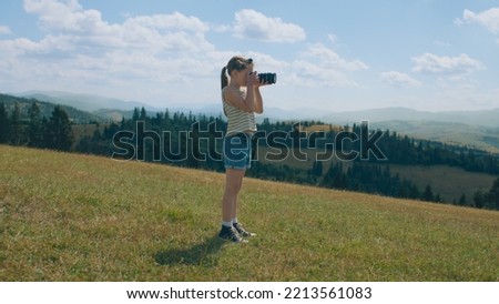Young photographer shooting landscape on beautifull green hillway, taking pictures of nature. Girl filling the portfolio with amazing photos, spending leisure time outdoor. Slow motion.