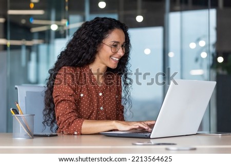 Young and happy hispanic woman working in modern office using laptop, business woman smiling and happy in glasses and curly hair Royalty-Free Stock Photo #2213564625