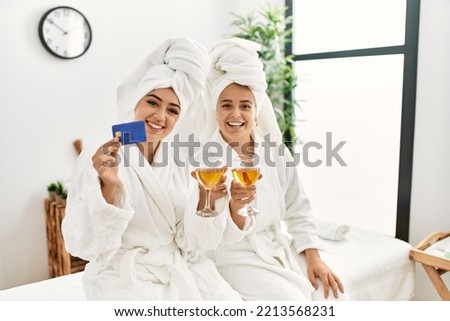 Woman couple holding credit card and toasting with champagne sitting on massage board at beauty center