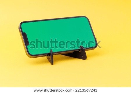 A smartphone standing on a black smartphone stand isolated on the yellow background