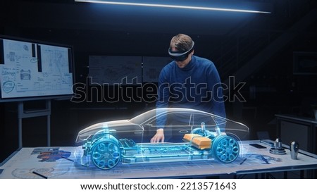 Automotive Engineer Wearing VR Headset Working on 3D Electric Car Prototype, Using Gestures in Augmented Reality. Designs and Manipulates Graphical Parts, Picks Body for the Chassis and Engine Royalty-Free Stock Photo #2213571643