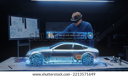 Automotive Engineer Wearing VR Headset Working on 3D Electric Car Prototype, Using Gestures in Augmented Reality. Manipulates Graphical Parts, Picks Body for the Chassis and Engine Royalty-Free Stock Photo #2213571649
