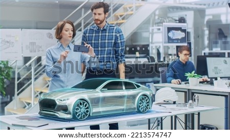 Industrial Design: Automotive Engineer and Designer Working Together on 3D Electric Car Design, Using Smartphone with Augmented Reality. Graphical Engine, Battery, Chassis, Body Collect into Vehicle