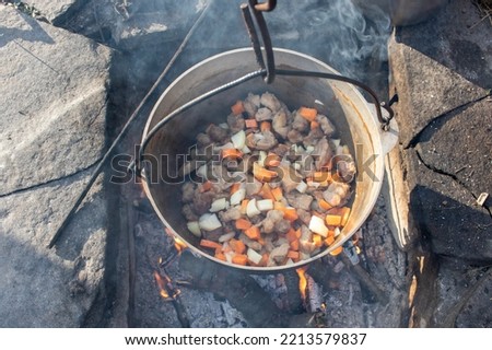 Cooking food in a cast iron cauldron on fire in camping. Baked meat with vegetables on bonfire. Top view. Cooking on campfire, picnic, camping, barbeque. Outdoor activity in wild environment. 