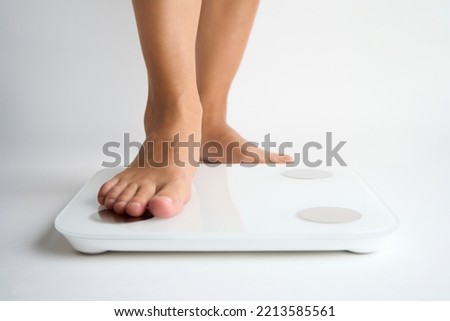 Woman legs stepping on floor scales, close-up. Female bare feet standing on scales, white background. Diet and overweight concept.  Royalty-Free Stock Photo #2213585561