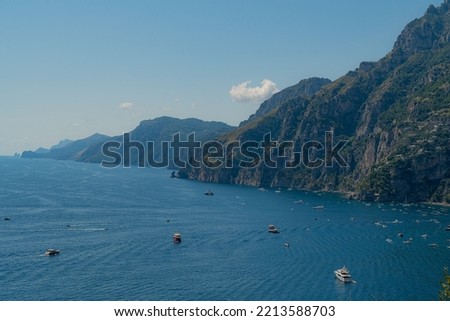Panoramic view of famous Amalfi coastline and mountain filled with boats carrying tourists.