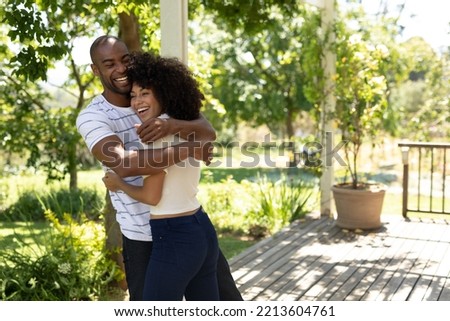 Weekend fun at home together. Side view of a mixed race couple standing on the patio in the sun, embracing and smiling