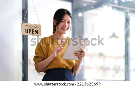 Happy young Asian woman owner standing holding a tablet with open sign board.