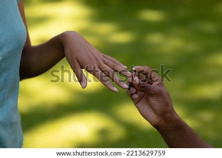 Close up of the hand of an African American man kneeling in the garden, proposing to his mixed race female partner and presenting her with an engagement ring Royalty-Free Stock Photo #2213629759