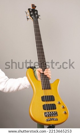 Vertical shot of a strong man hand holding a bass guitar with five chords. Studio shot over light grey background. Royalty-Free Stock Photo #2213665253