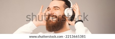 Close up panorama shot of a bearded man enjoying music through headphones. Studio photo.