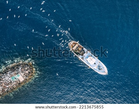 Top view of a fishing trawler coming back to the port and the seagulls are flying over it. Royalty-Free Stock Photo #2213675855