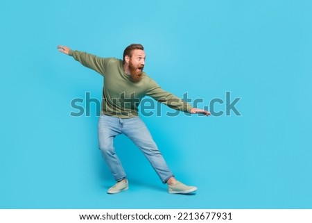 Full size photo of attractive young guy surfing invisible wave have fun dancing fooling wear khaki look isolated on cyan color background