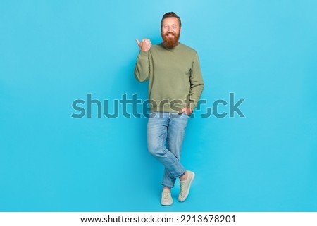 Full length photo of optimistic guy ginger hairdo khaki long sleeve directing empty space hand in pocket isolated on blue color background