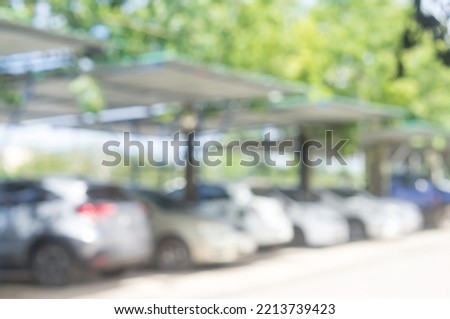 Cars are parking at parking lot with roof in open area in front of office, university, school or hospital on sunny day. Blurred photo