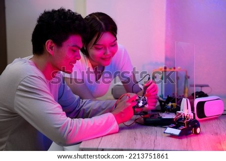 Young man and young woman amateur inventor testing electronic device model inventions with in black light mood. Royalty-Free Stock Photo #2213751861