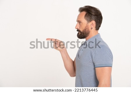 Profile bearded serious man pointing finger to the side at space stands on isolated white background
