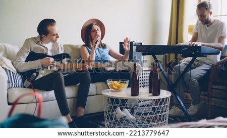 Young friends musicians are practising at home singing and playing guitar and keyboard. Musical instruments, attractive creative people, friendship and hobby concept.
