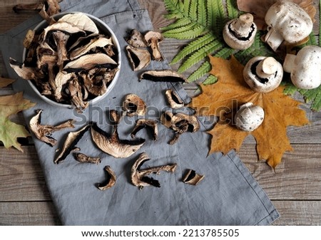 Dried and fresh champignon mushrooms in a bowl and on a cutting kitchen board. The idea of natural organic ecological products and their preparation for future use for autumn and winter. Royalty-Free Stock Photo #2213785505
