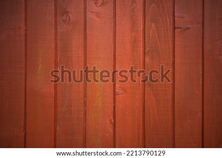 Photo of a wooden wall of a country house. The background is made of wood painted with rowan-colored paint. Fence made of red boards