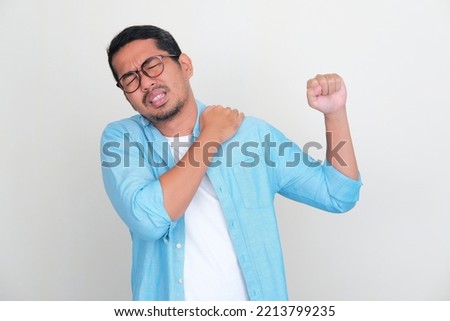 Adult Asian man touching his left shoulder with pain expression