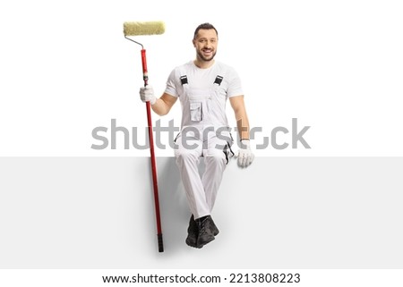 Painter holding a paint roller and sitting on a blank panel isolated on white background Royalty-Free Stock Photo #2213808223
