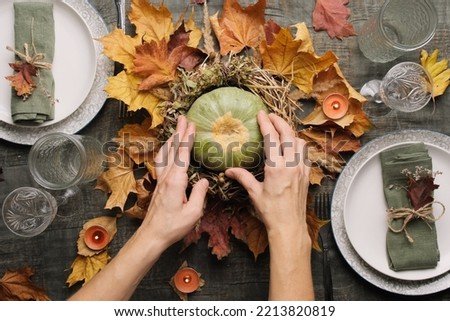 Hands makes autumn arrangement with pumpkin for thanksgiving holiday feast. Autumnal table setting for holiday dinner, top view. 