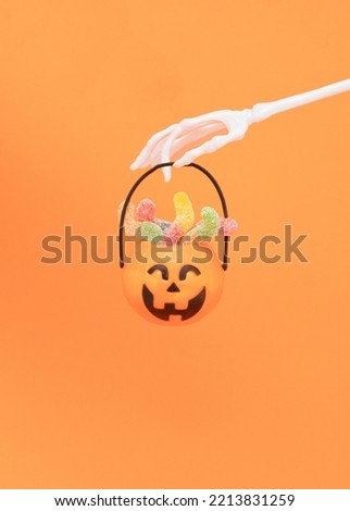 Skeleton hand hold scary pumpkin with colorful candy worm. Halloween trick or treat concept on orange background.