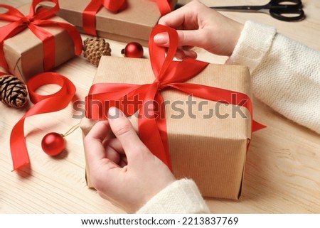 Christmas present. Woman tying ribbon bow on gift box at wooden table, closeup